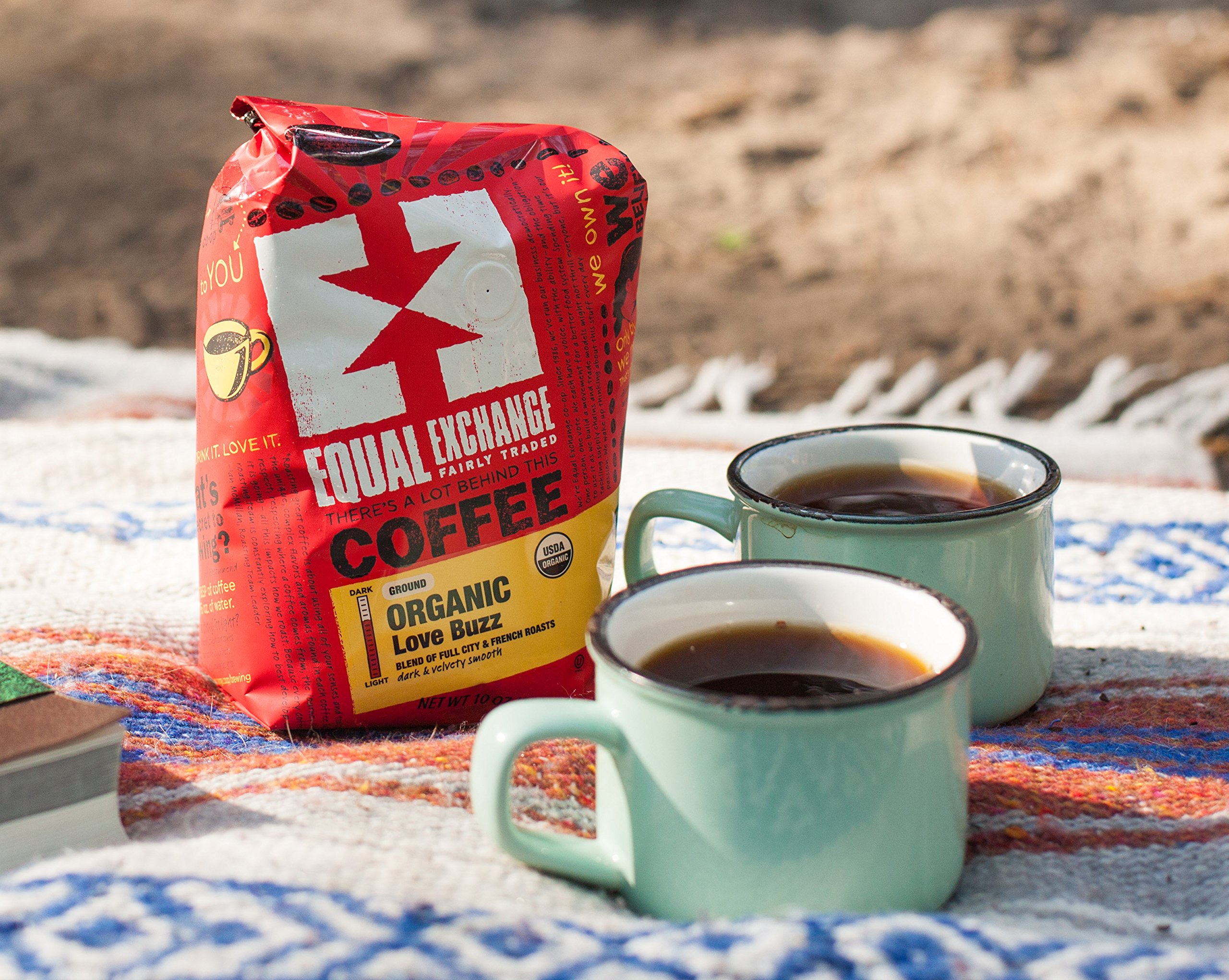 A bag of coffee and two mugs of coffee on a blanket